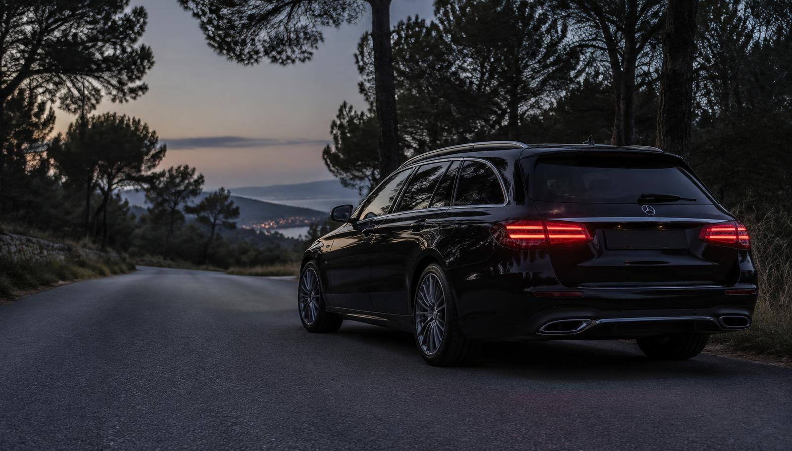 Carrinha Mercedes-Benz Classe E preta numa estrada arborizada ao entardecer, com as luzes traseiras acesas